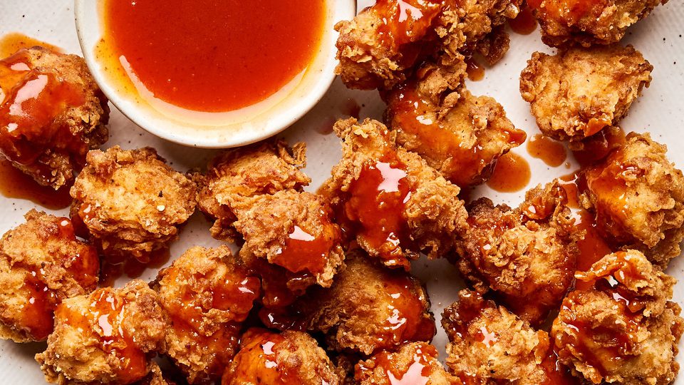 Crispy hot honey chicken nuggets drizzled with spicy sweet glaze on a plate, served with extra hot honey sauce for dipping