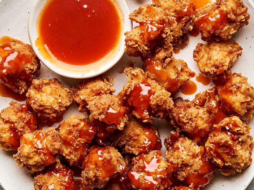 Crispy hot honey chicken nuggets drizzled with spicy sweet glaze on a plate, served with extra hot honey sauce for dipping