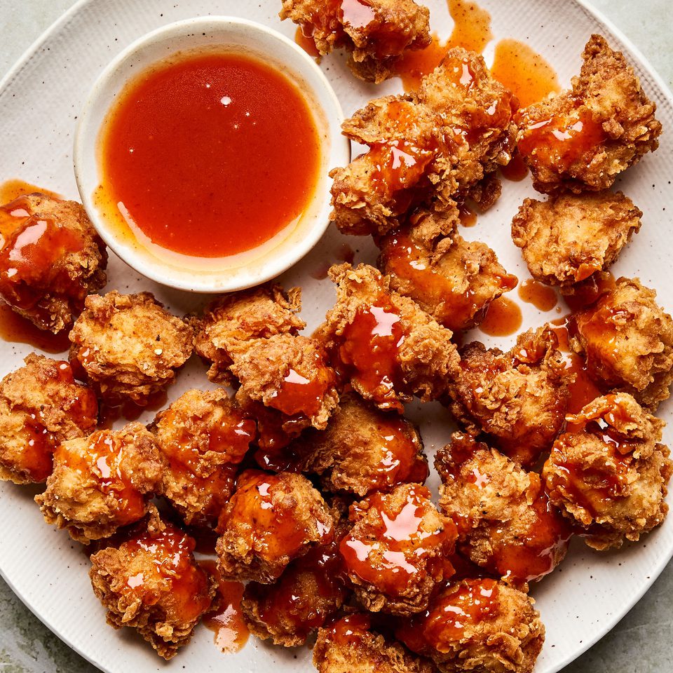 Crispy hot honey chicken nuggets drizzled with spicy sweet glaze on a plate, served with extra hot honey sauce for dipping