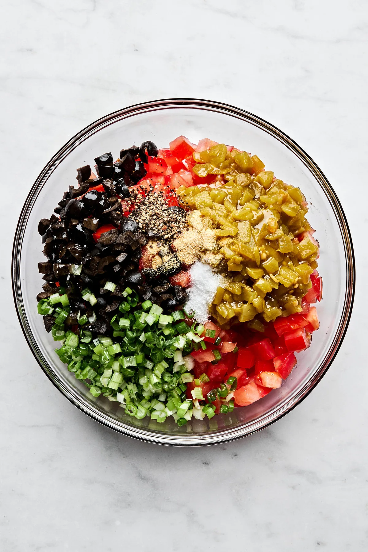 A vibrant tomato and olive salsa being made in a bowl, featuring diced tomatoes, black olives, and chiles