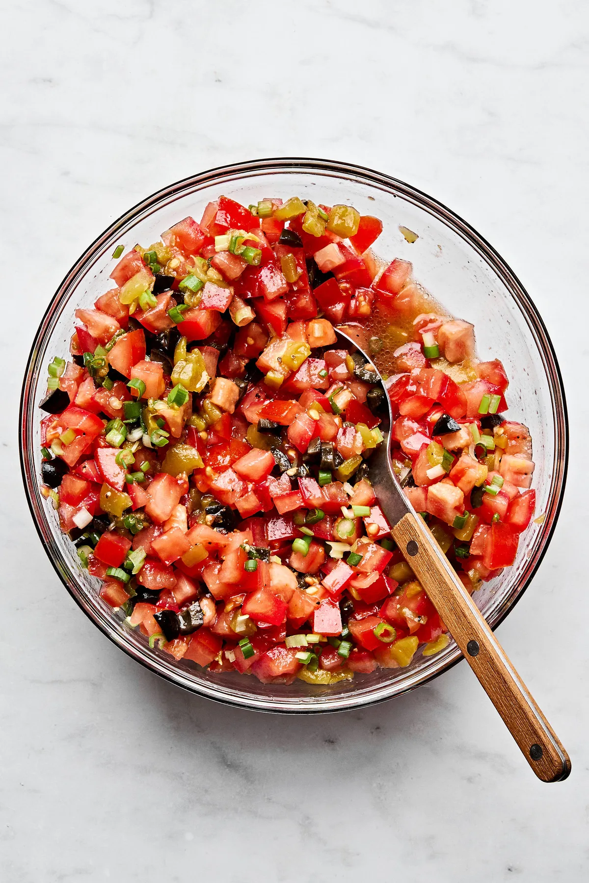 A vibrant tomato and olive salsa being stirred in a bowl, featuring diced tomatoes, black olives, and chiles