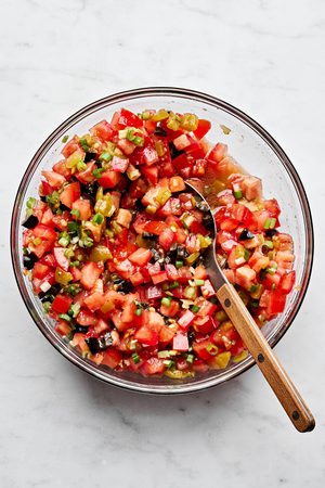 A vibrant tomato and olive salsa being stirred in a bowl, featuring diced tomatoes, black olives, and chiles
