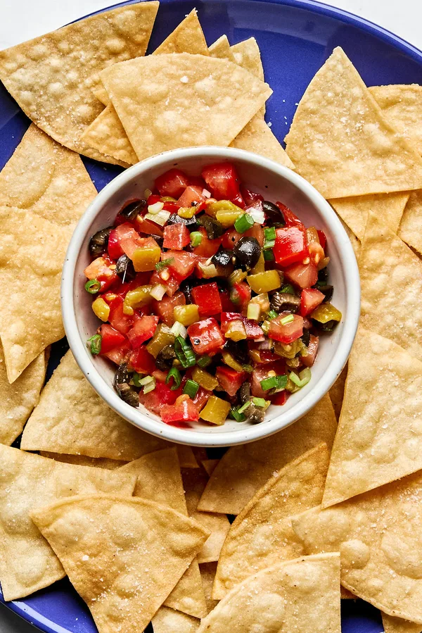 A vibrant tomato and olive salsa in a white bowl, featuring diced tomatoes, black olives, and chiles, served with chips