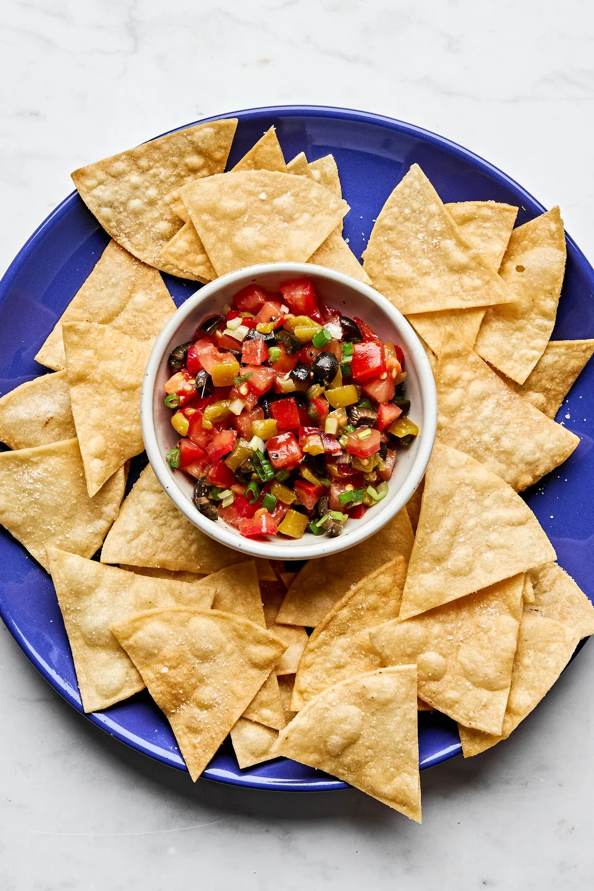 A vibrant tomato and olive salsa in a white bowl, featuring diced tomatoes, black olives, and chiles, served with chips