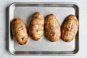 4 baked potatoes on a rimmed baking sheet