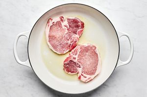 pork chops seasoned with salt being cooked in olive oil in a skillet