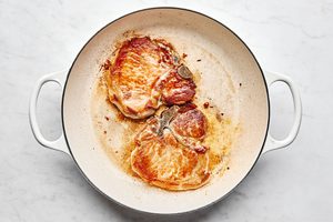 pork chops seasoned with salt being cooked in olive oil in a skillet