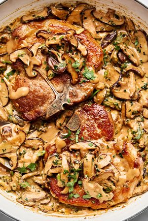 Pork chops with miso mushrooms in a creamy sauce with cilantro and green onions in a skillet