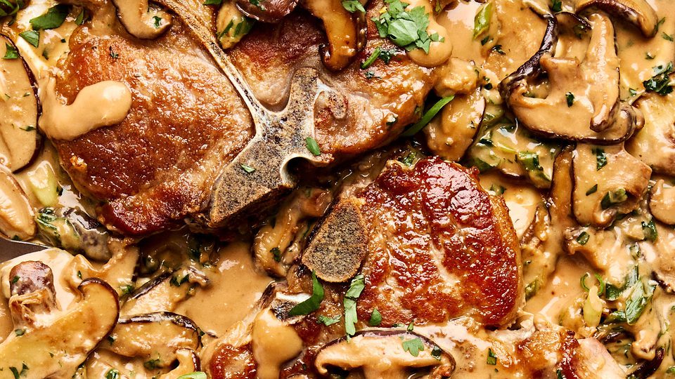 Pork chops with miso mushrooms in a creamy sauce with cilantro and green onions in a skillet
