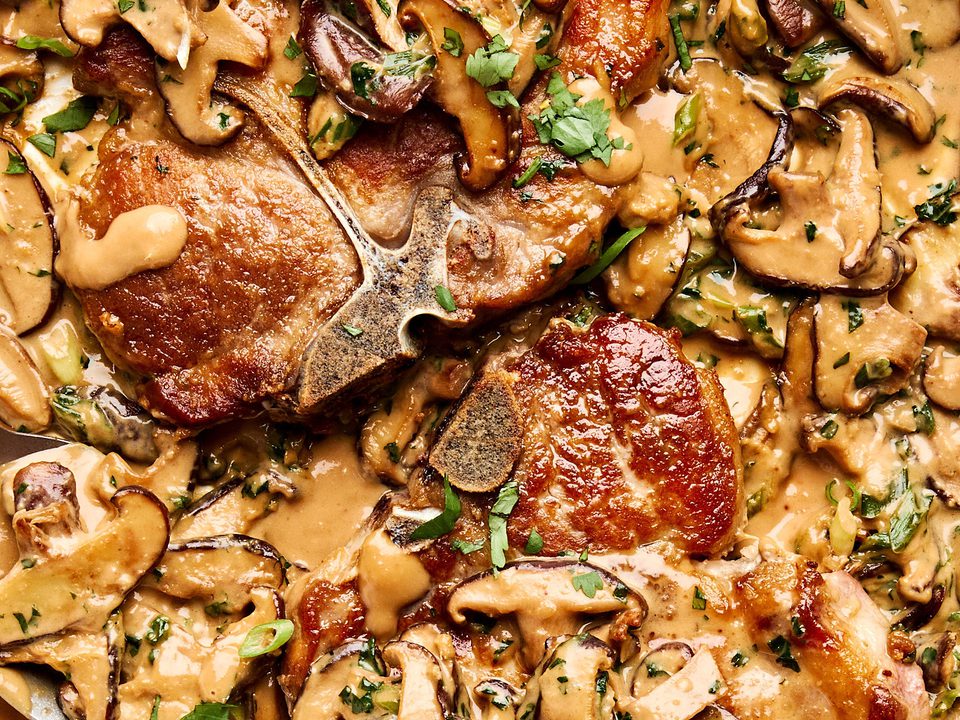 Pork chops with miso mushrooms in a creamy sauce with cilantro and green onions in a skillet