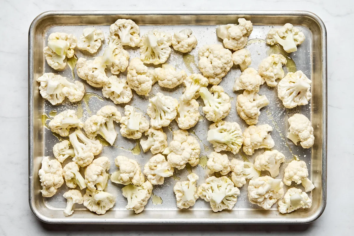 chopped cauliflower tossed with olive oil and salt on a baking sheet ready to be roasted