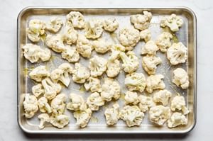 chopped cauliflower tossed with olive oil and salt on a baking sheet ready to be roasted
