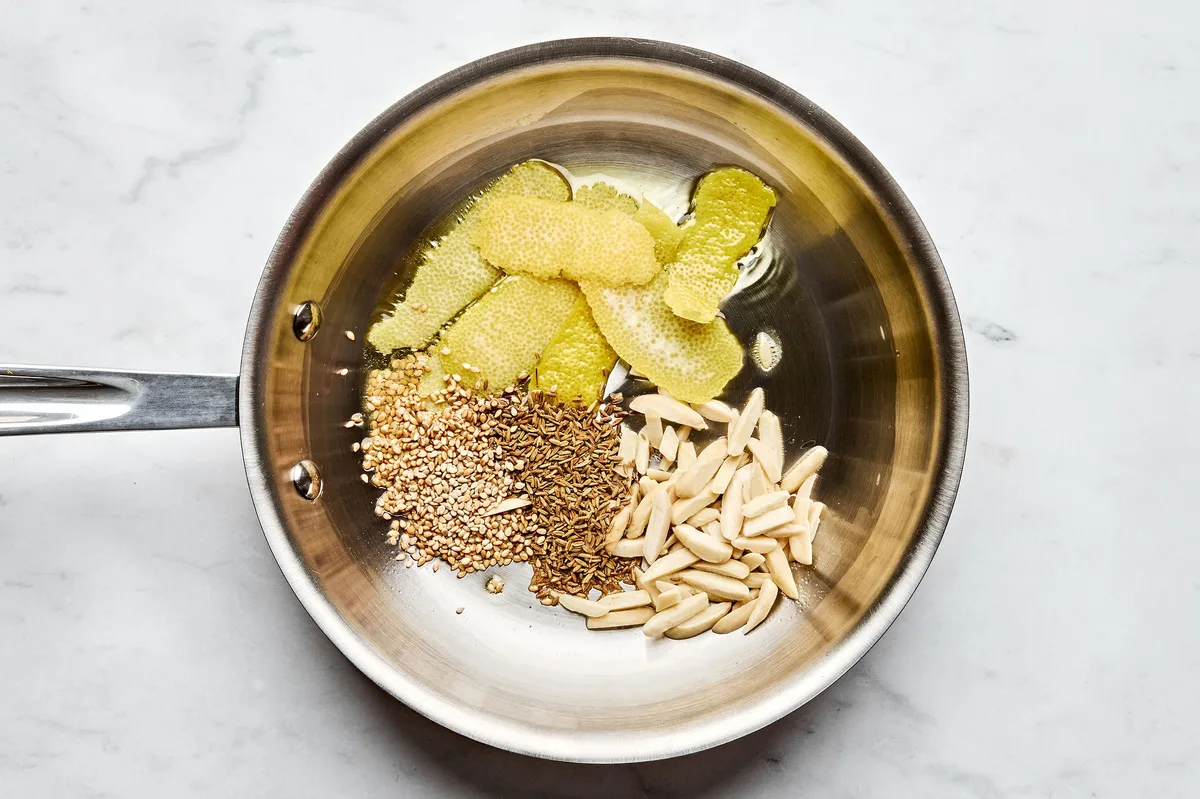 lemon peel, almonds, cumin seeds, and sesame seeds cooking in olive oil in a skillet