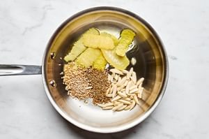 lemon peel, almonds, cumin seeds, and sesame seeds cooking in olive oil in a skillet