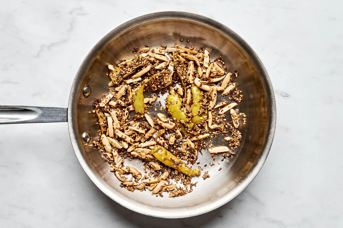 lemon peel, almonds, cumin seeds, and sesame seeds cooking in olive oil in a skillet