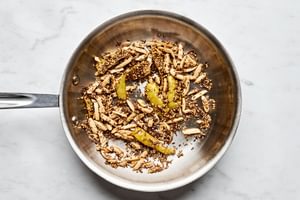 lemon peel, almonds, cumin seeds, and sesame seeds cooking in olive oil in a skillet