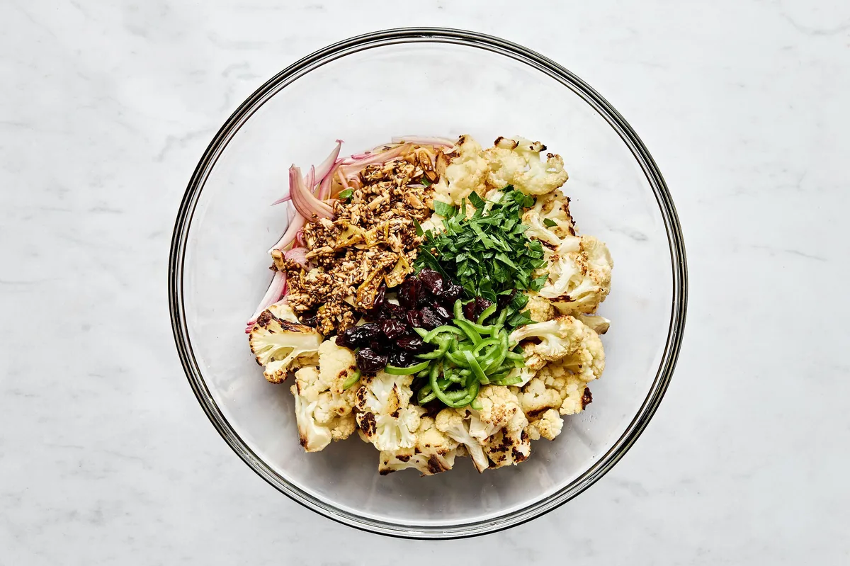 Roasted cauliflower, herbs, almonds, dried cherries, and spices being tossed in a bowl to make roasted cauliflower salad