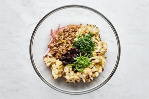 Roasted cauliflower, herbs, almonds, dried cherries, and spices being tossed in a bowl to make roasted cauliflower salad