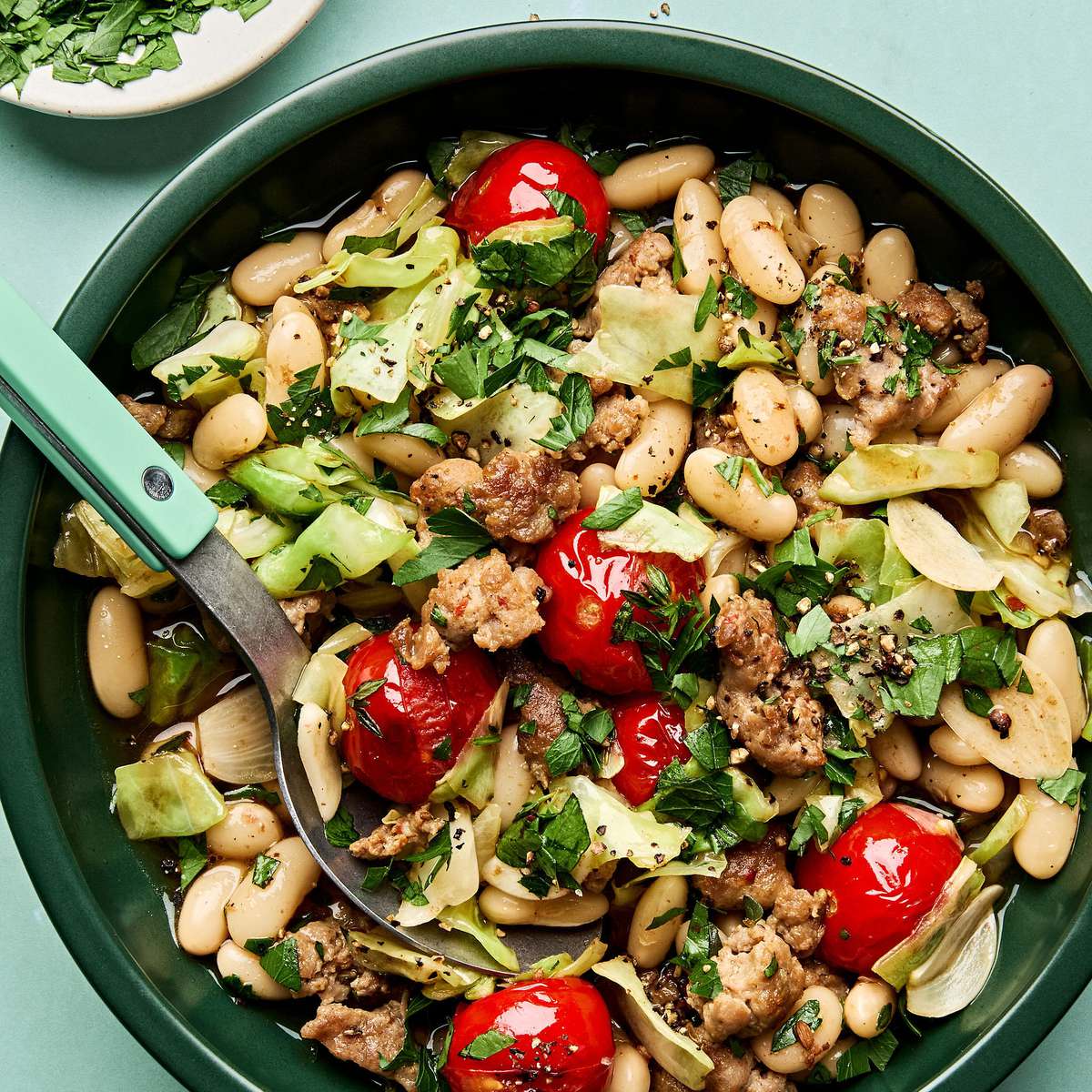 Italian sausage, cabbage, and white bean skillet served in a bowl with cherry tomatoes and fresh herbs, hearty one-pan dinner