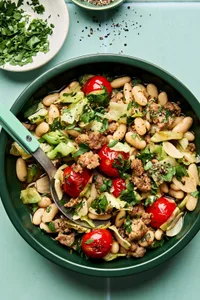 Italian sausage, cabbage, and white bean skillet served in a bowl with cherry tomatoes and fresh herbs, hearty one-pan dinner