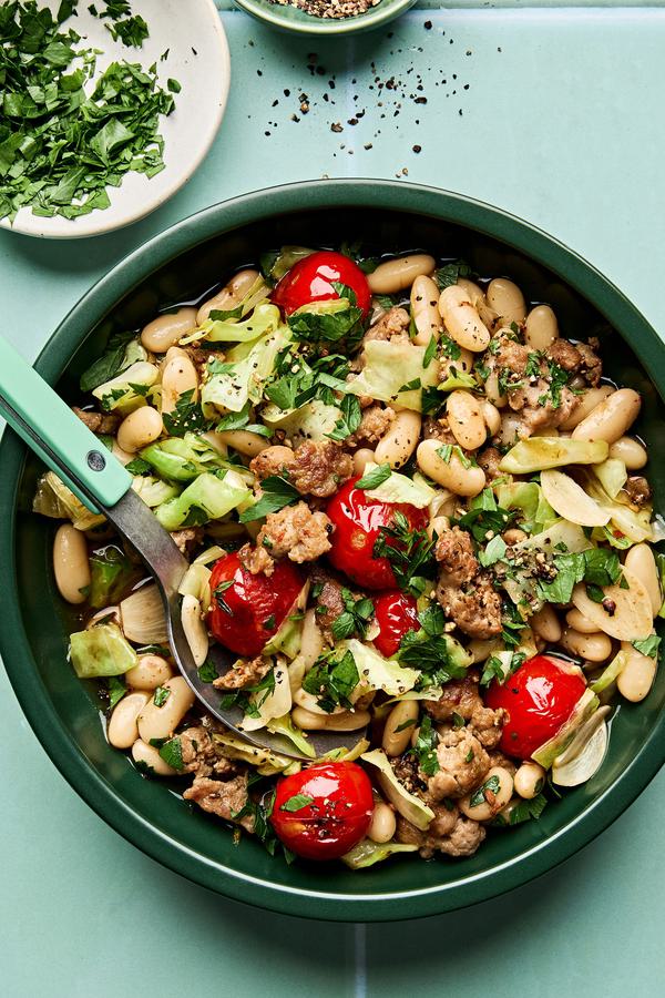 Italian sausage, cabbage, and white bean skillet served in a bowl with cherry tomatoes and fresh herbs, hearty one-pan dinner