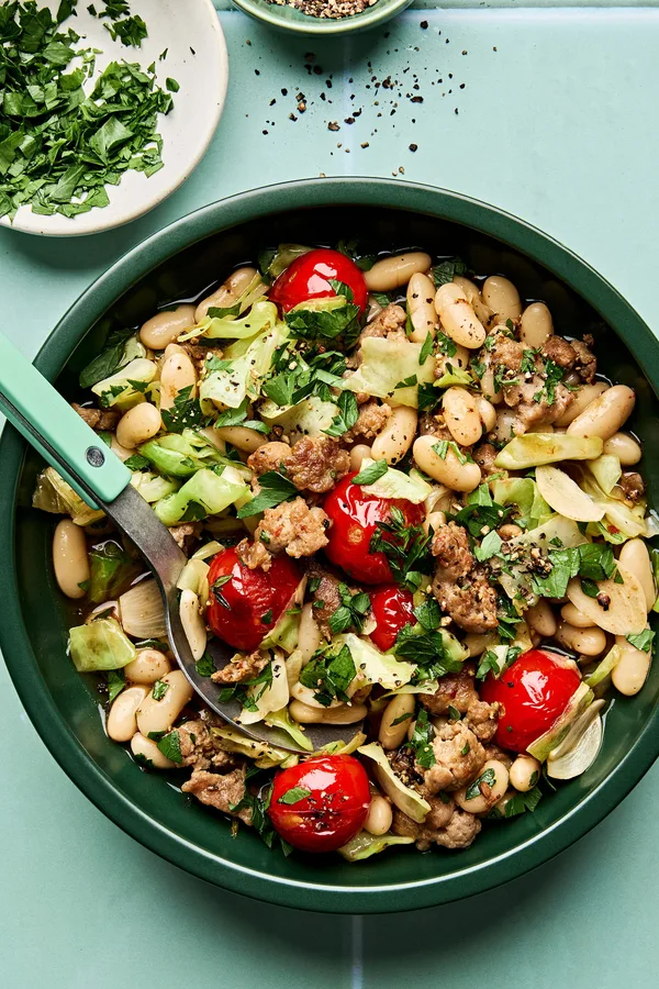 Italian sausage, cabbage, and white bean skillet served in a bowl with cherry tomatoes and fresh herbs, hearty one-pan dinner