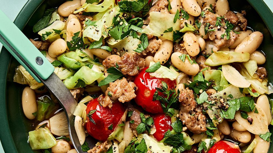 Italian sausage, cabbage, and white bean skillet served in a bowl with cherry tomatoes and fresh herbs, hearty one-pan dinner