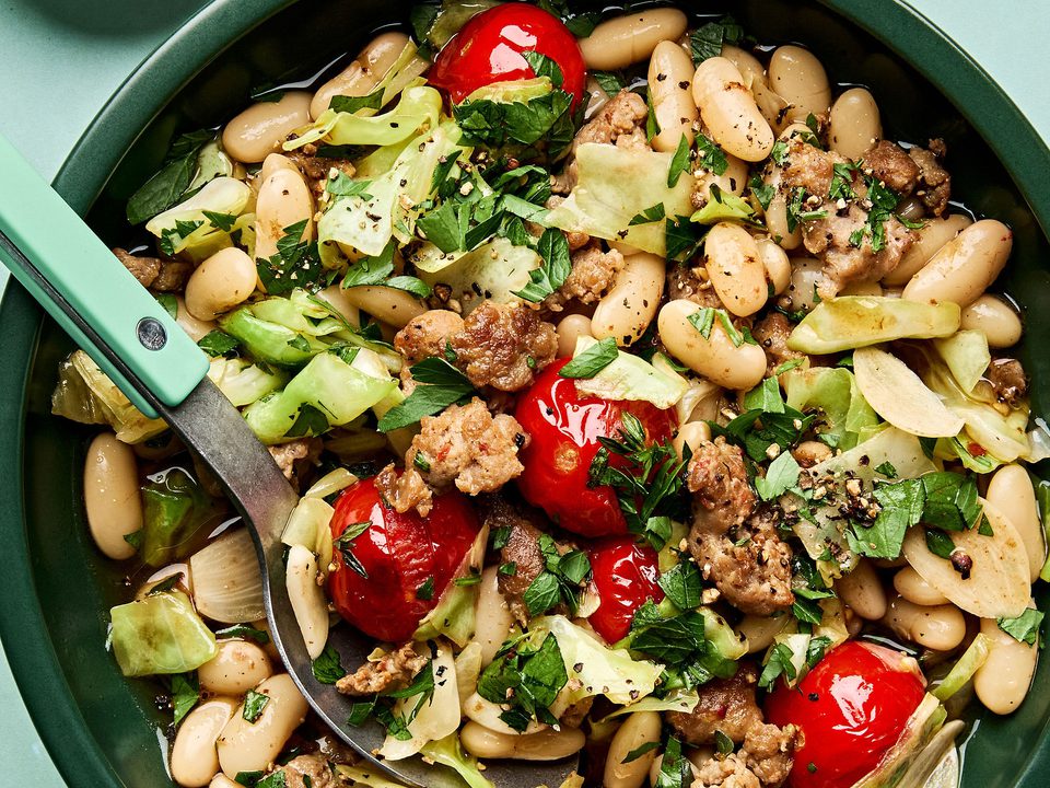 Italian sausage, cabbage, and white bean skillet served in a bowl with cherry tomatoes and fresh herbs, hearty one-pan dinner