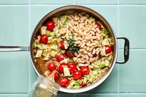 ground italian chicken sausage, chopped cabbage and white beans cooking in a skillet with cherry tomatoes, broth & herbs