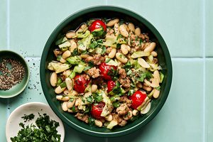 Italian sausage, cabbage, and white bean skillet served in a bowl with cherry tomatoes and fresh herbs, hearty one-pan dinner