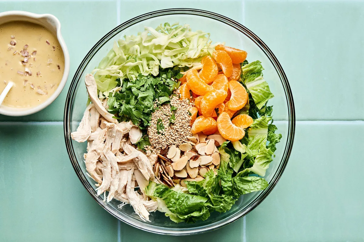 a sesame chicken salad with juicy orange slices and sliced almonds with a homemade miso dressing being tossed in a bowl