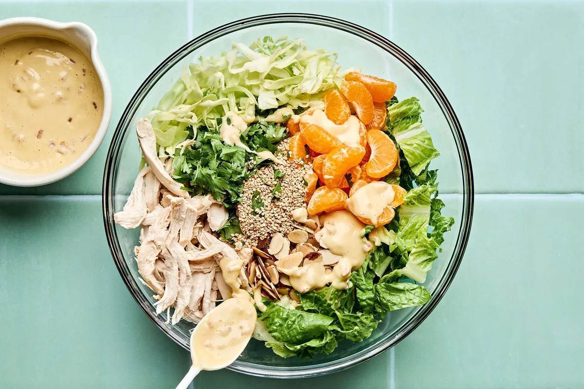 a sesame chicken salad with juicy orange slices and sliced almonds with a homemade miso dressing being tossed in a bowl