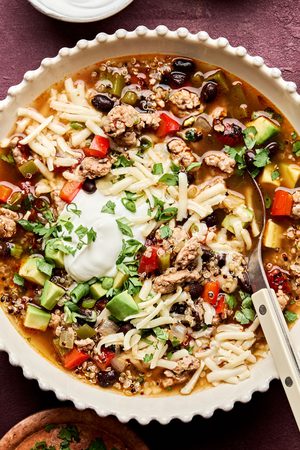 Bowl of Healthy Southwest turkey quinoa soup topped with sour cream, avocado, cilantro, and green onion. A hearty dinner.