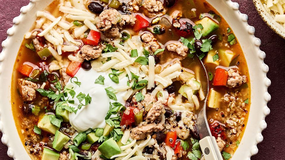 Bowl of Healthy Southwest turkey quinoa soup topped with sour cream, avocado, cilantro, and green onion. A hearty dinner.