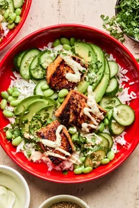 Teriyaki Salmon Bowl with coconut rice, edamame, cucumbers, avocado, cilantro and sesame seeds drizzled with wasabi dressing