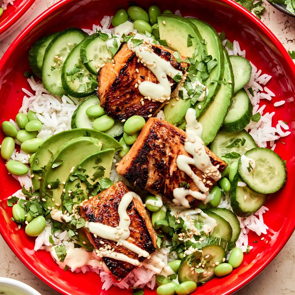 Teriyaki Salmon Bowl with coconut rice, edamame, cucumbers, avocado, cilantro and sesame seeds drizzled with wasabi dressing