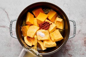 garlic, ginger, onions, red curry paste, pumpkin, squash, stock and salt being boiled in a pot to make Thai pumpkin soup