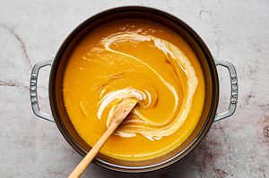 coconut milk and fish sauce being stirred into a pot of creamy thai pumpkin soup, perfect for a fall dinner