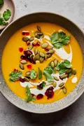 a bowl of Thai pumpkin soup topped with sriracha, pumpkin seeds and cilantro, a perfect cozy soup for fall