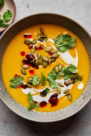 a bowl of Thai pumpkin soup topped with sriracha, pumpkin seeds and cilantro, a perfect cozy soup for fall