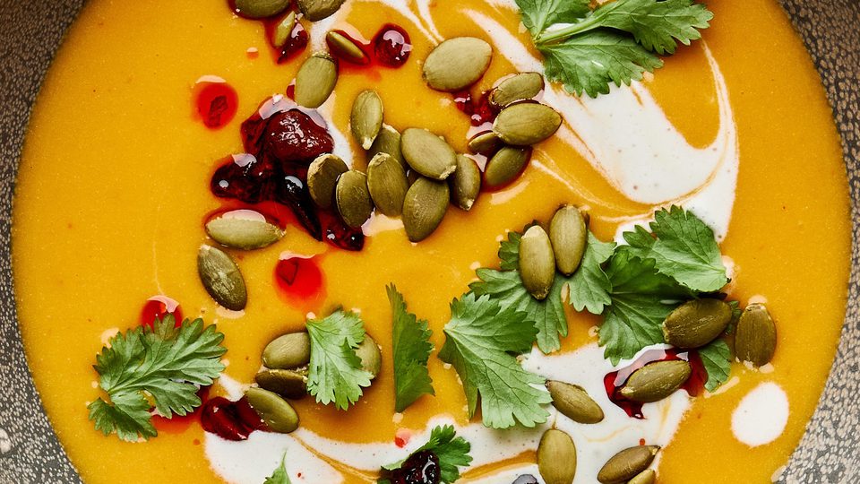 a bowl of Thai pumpkin soup topped with sriracha, pumpkin seeds and cilantro, a perfect cozy soup for fall