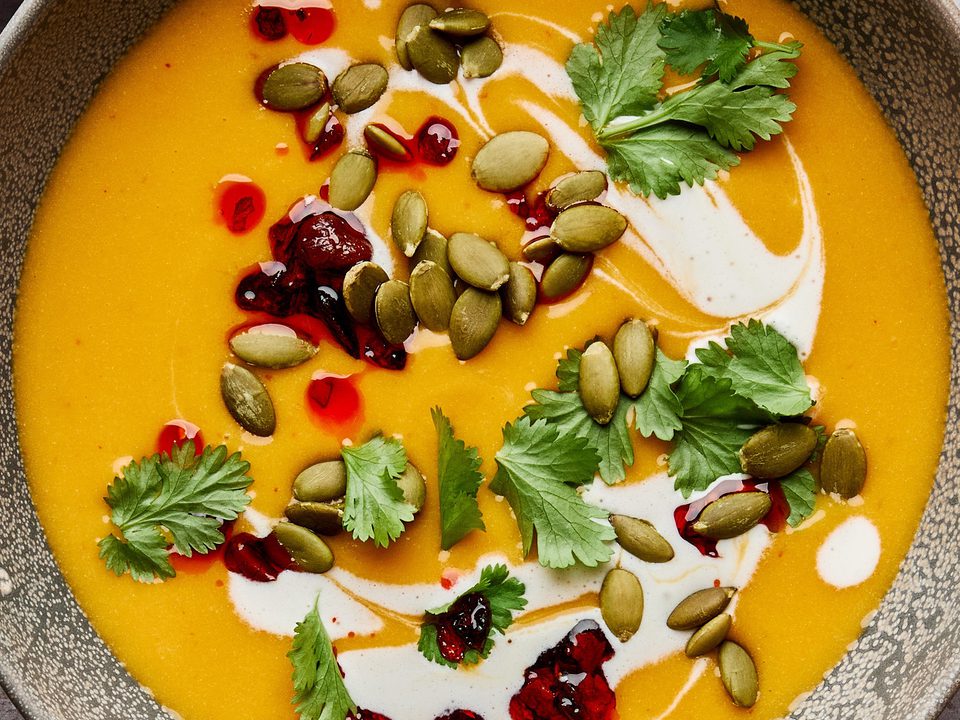 a bowl of Thai pumpkin soup topped with sriracha, pumpkin seeds and cilantro, a perfect cozy soup for fall