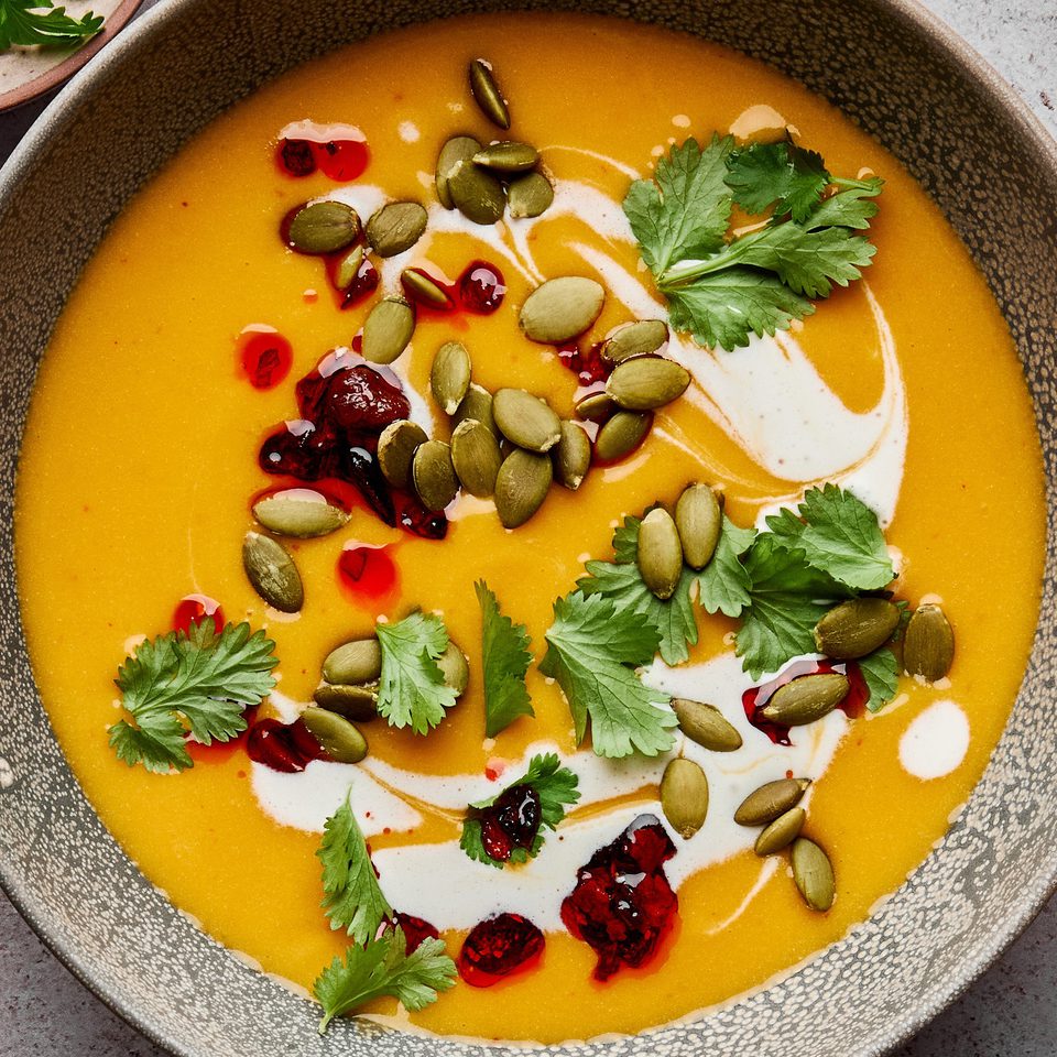 a bowl of Thai pumpkin soup topped with sriracha, pumpkin seeds and cilantro, a perfect cozy soup for fall