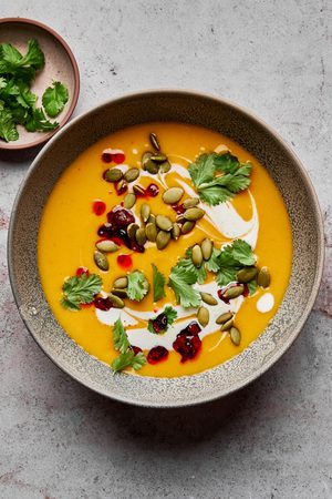 a bowl of Thai pumpkin soup topped with sriracha, pumpkin seeds and cilantro, a perfect cozy soup for fall