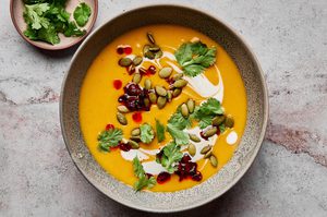 a bowl of Thai pumpkin soup topped with sriracha, pumpkin seeds and cilantro, a perfect cozy soup for fall