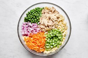 pasta, peas, red onion, celery and carrots being tossed in a bowl to make tuna pasta salad
