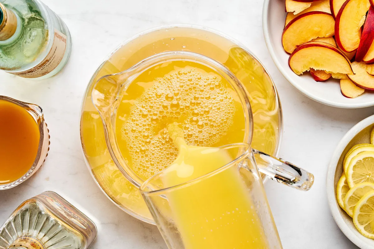 wine, orange juice, triple sec, and peach nectar being stirred into a glass pitcher to make white sangria