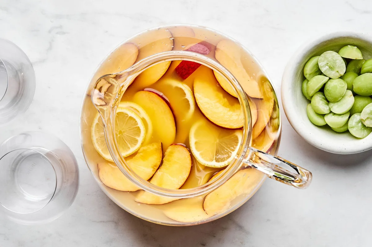 sliced peaches and lemons added to a pitcher with wine, orange juice, triple sec, and peach nectar