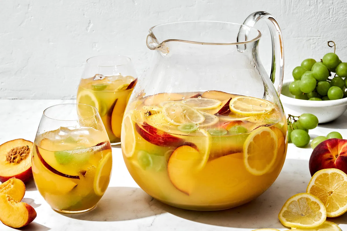 a large pitcher of white sangria filled with fruit slices, surrounded by glasses of sangria