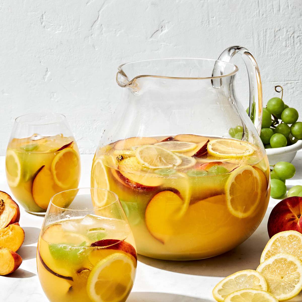 a large pitcher of white sangria filled with fruit slices, surrounded by glasses of sangria